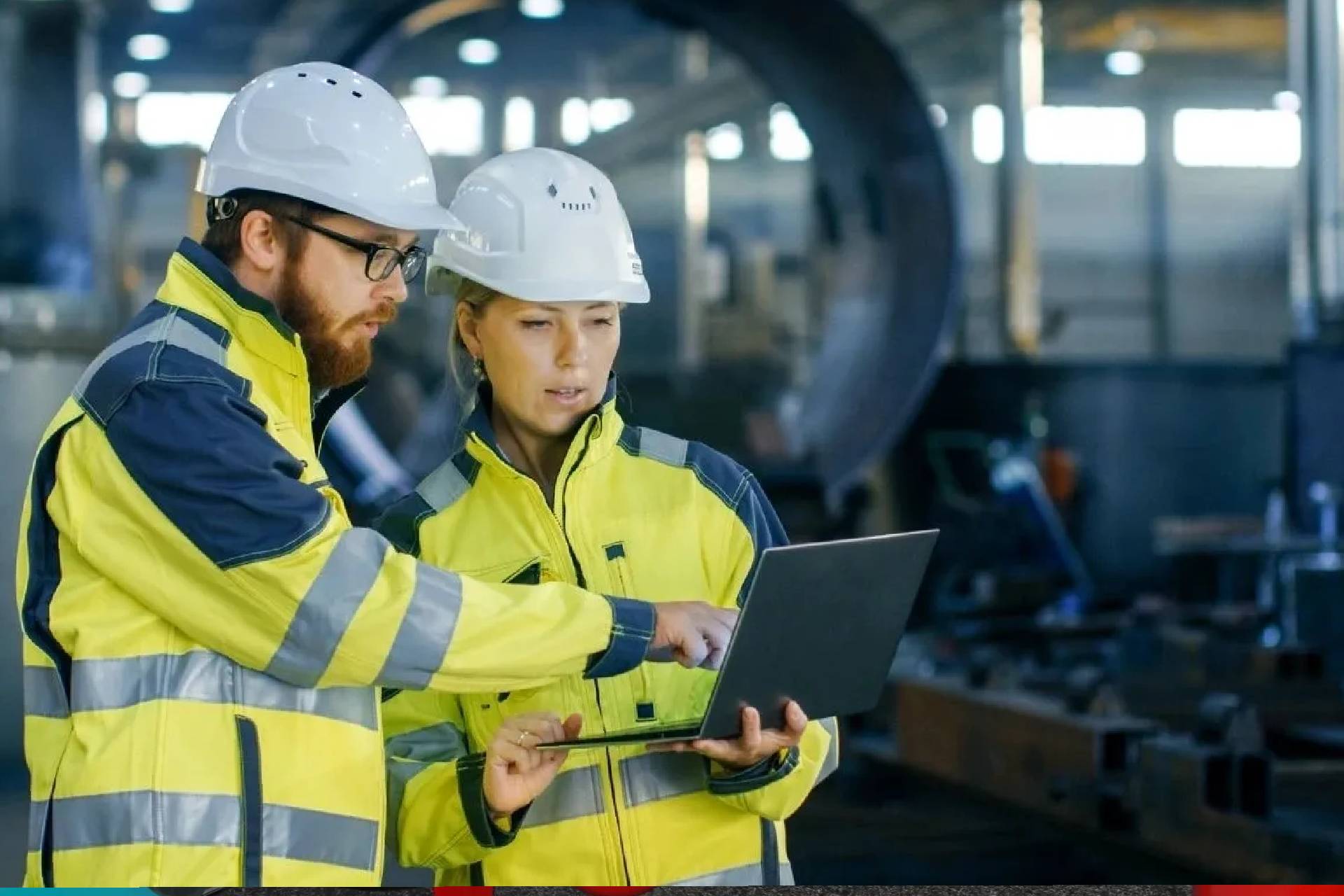 Two people in hard hats and yellow jackets looking at a laptop.