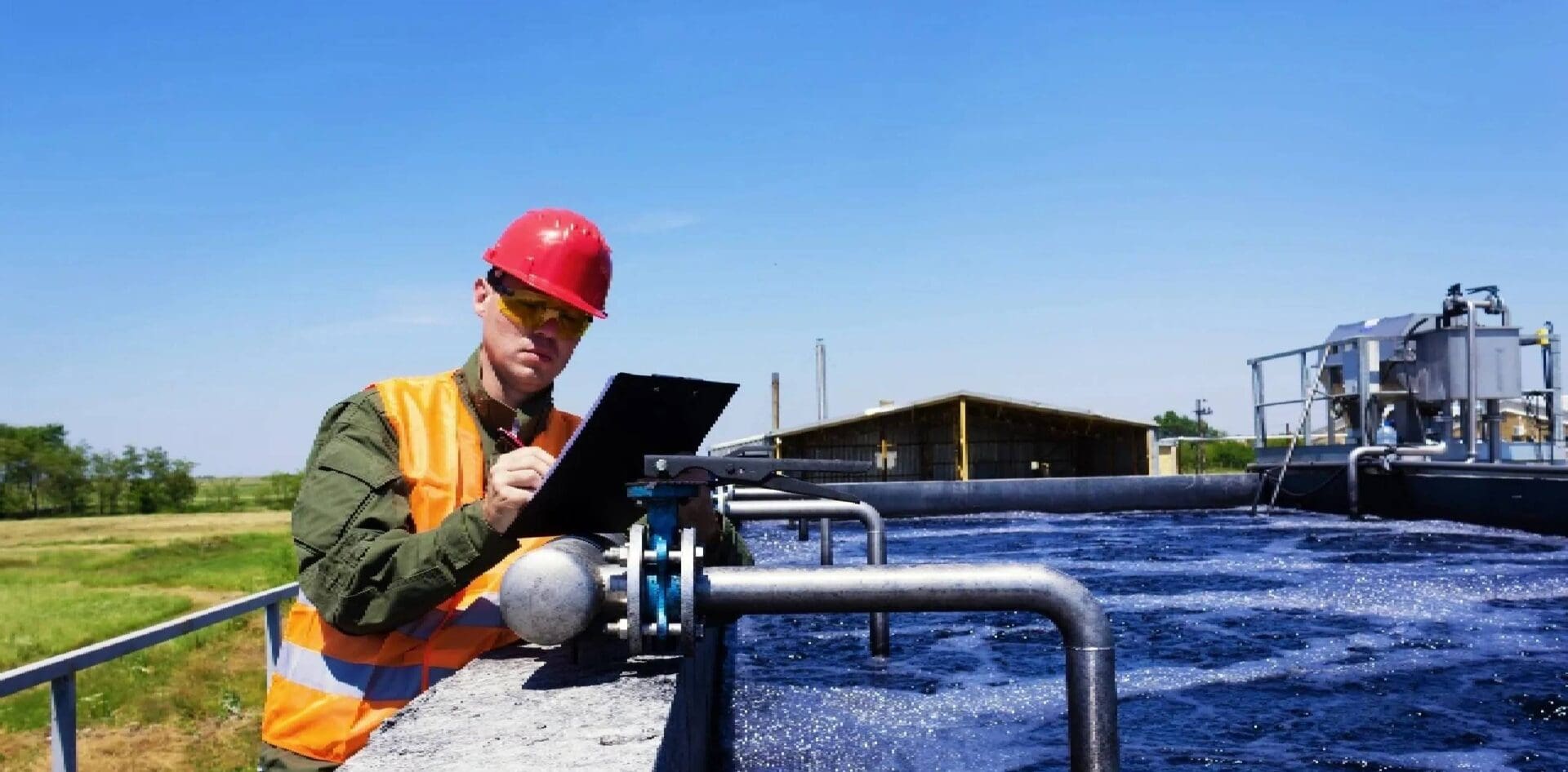 A man in an orange hard hat is writing on his clipboard.